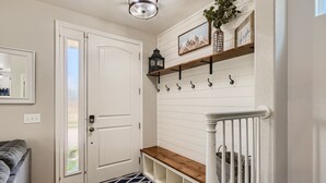 A hallway with a white door, a bench, a hanging lantern, and a shelf with hooks.