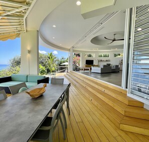 A modern living room with a large TV, comfortable seating, and a view of the outdoors. - Villa Menemene | Punaauia • Private Pool • Moorea View • 4 Bedrooms (PUNAAUIA)