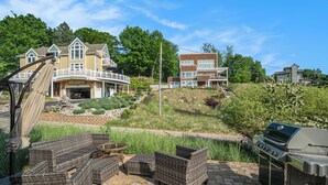 Eine Terrasse mit Korbmöbeln, einem Grill und einem Haus mit großer Garage und Balkon.