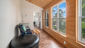 Ein modernes Interieur mit Holzvertäfelung, großen Fenstern, einem Ledersitzhocker und einem Sessel mit gemustertem Kissen.