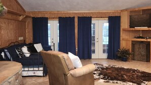 Ein gemütliches Wohnzimmer mit einer Couch, einem braunen Sessel, einer Steinwand, einem Kuhfellteppich und einem Fernseher auf einer Holzkommode.