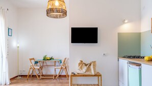 A compact kitchen with a TV, a dining area with chairs and a table, and a small bench.