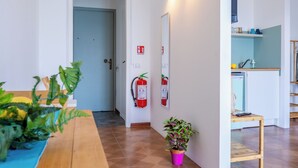 A hotel hallway with a wooden table, potted plants, a fire extinguisher, and a mirror on the wall.