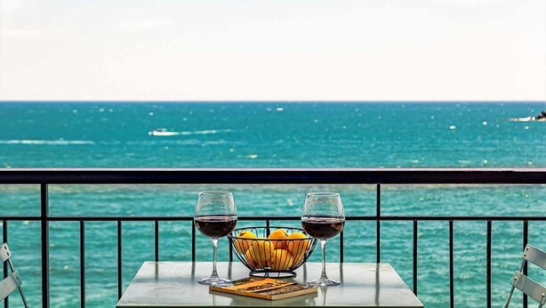 Ein Tisch mit zwei Weingläsern und einer Obstschale auf einem Balkon mit Blick aufs Meer.