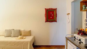 Ein Schlafzimmer mit Bett, Kissen, einem Hut, einem Bild mit rotem Rahmen, einem Herd und einem Obstkorb.