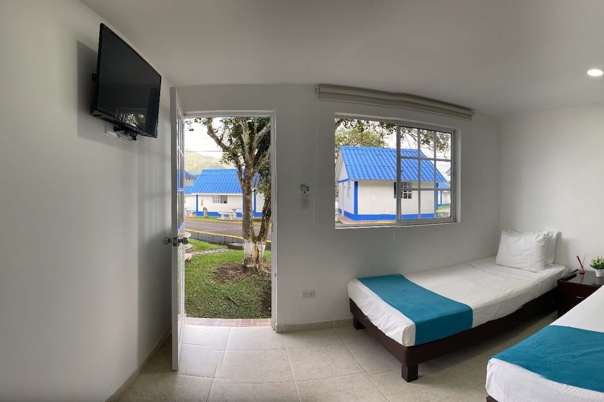 Habitación de hotel con dos camas, televisión y ventana con vistas a edificios y un árbol.