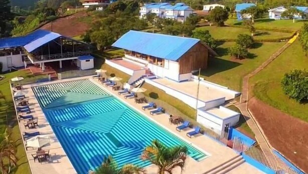 Vista aérea de un resort con una amplia piscina, tumbonas y una zona cubierta con techo azul.