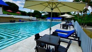 Zona junto a la piscina con sillones de descanso y sombrillas, un suelo de baldosas y vistas a la piscina y la vegetación circundante.
