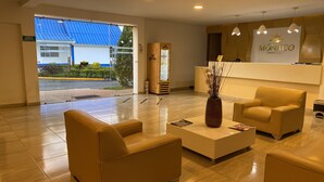 Zona de recepción de un hotel con un mostrador, dos sillones, una mesita de centro y un florero.