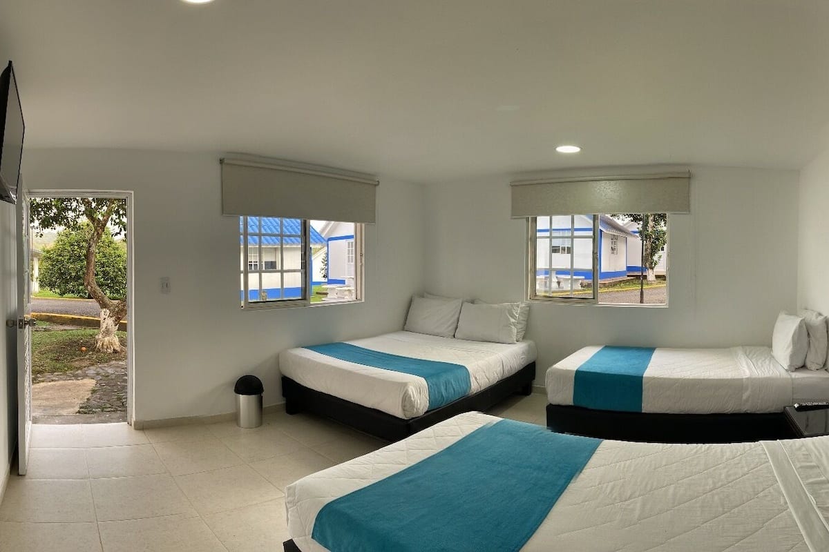 Habitación de hotel con tres camas, televisión y ventanas con persianas.
