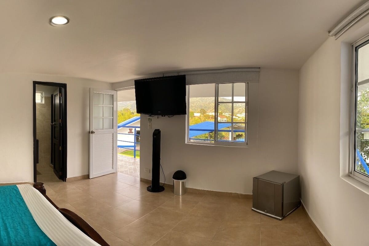 Un dormitorio con cama, televisión, ventana y puerta que da a un balcón.