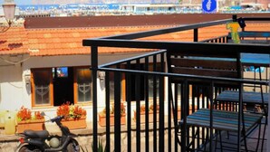 Un bâtiment situé sur la côte, avec un toit recouvert de tuiles rouges, un balcon doté de rampes en métal et un scooter garé devant.