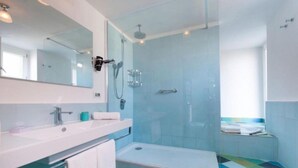 Un baño moderno con cabina de ducha de vidrio, un lavabo blanco y un suelo colorido.