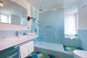 Un baño moderno con cabina de ducha de vidrio, un lavabo blanco y un suelo colorido.