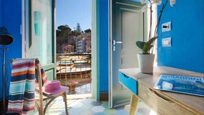 Una habitación con vista al puerto, una silla con toalla a rayas, una planta en maceta y una revista sobre la mesa.