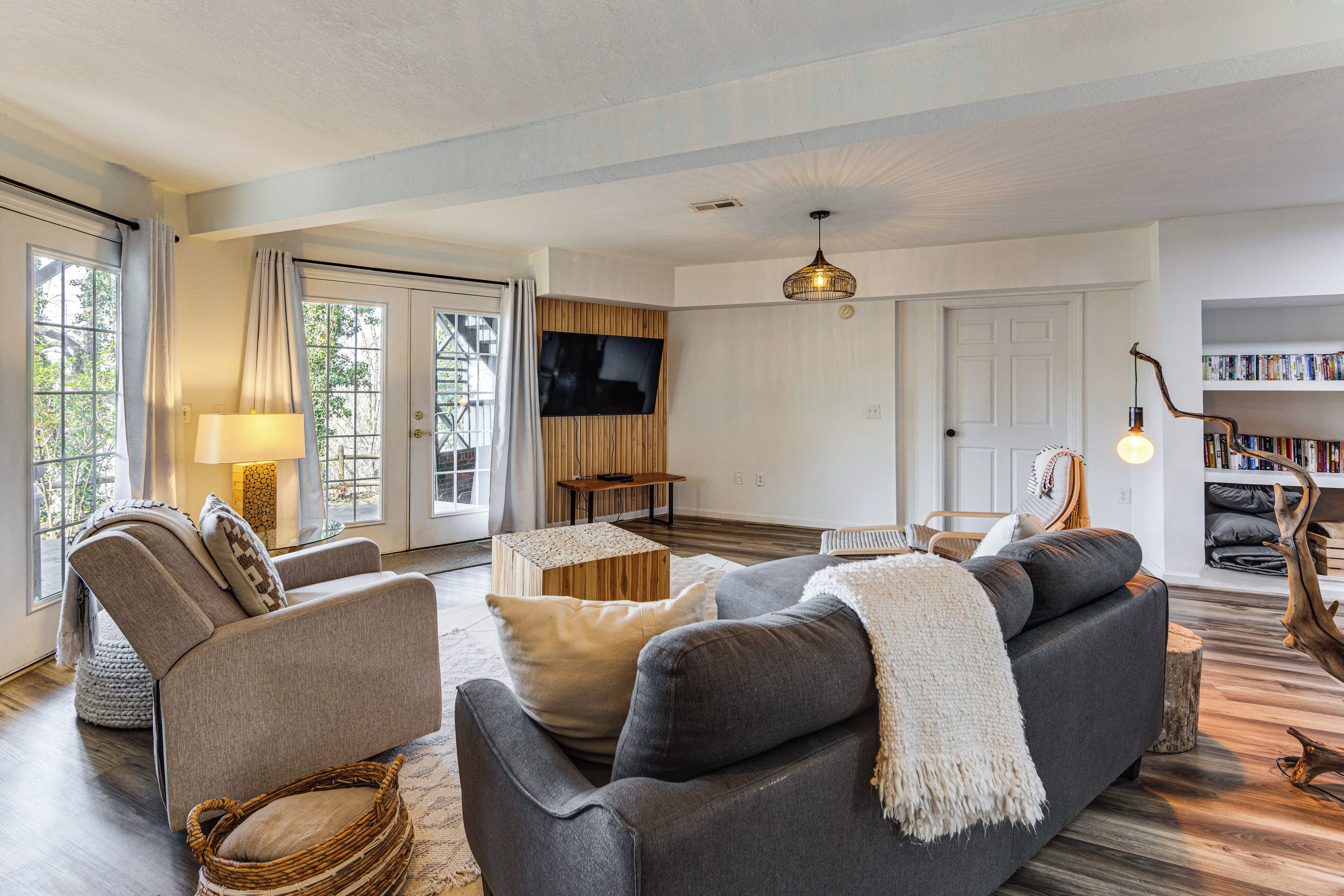 A living room with a sofa, armchairs, a TV, a bookshelf, and a wooden floor.