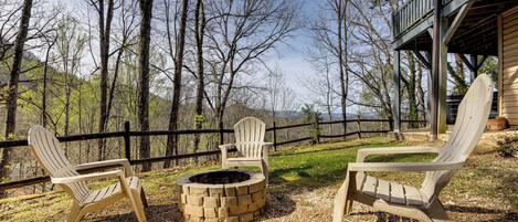A deck with Adirondack chairs and a fire pit, surrounded by trees and a wooden fence.