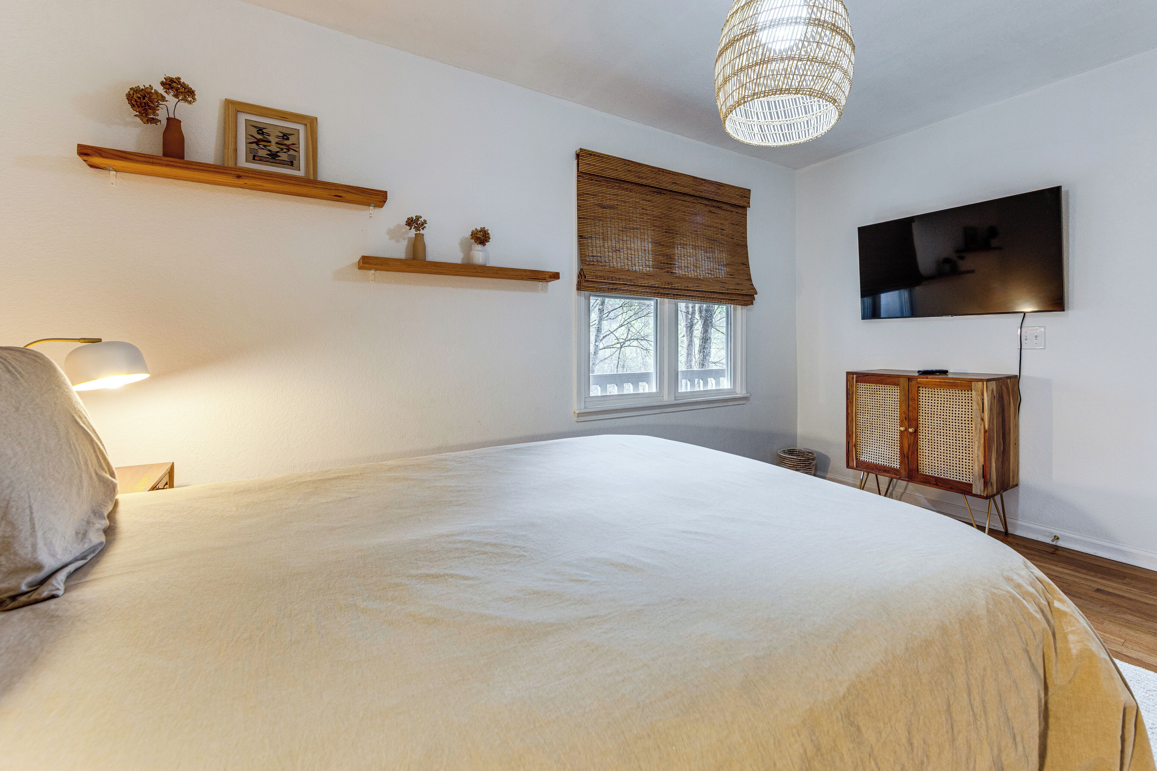 Ein Schlafzimmer mit einem großen Bett, einem Fernseher, einer Korblampe und Holzregalen.