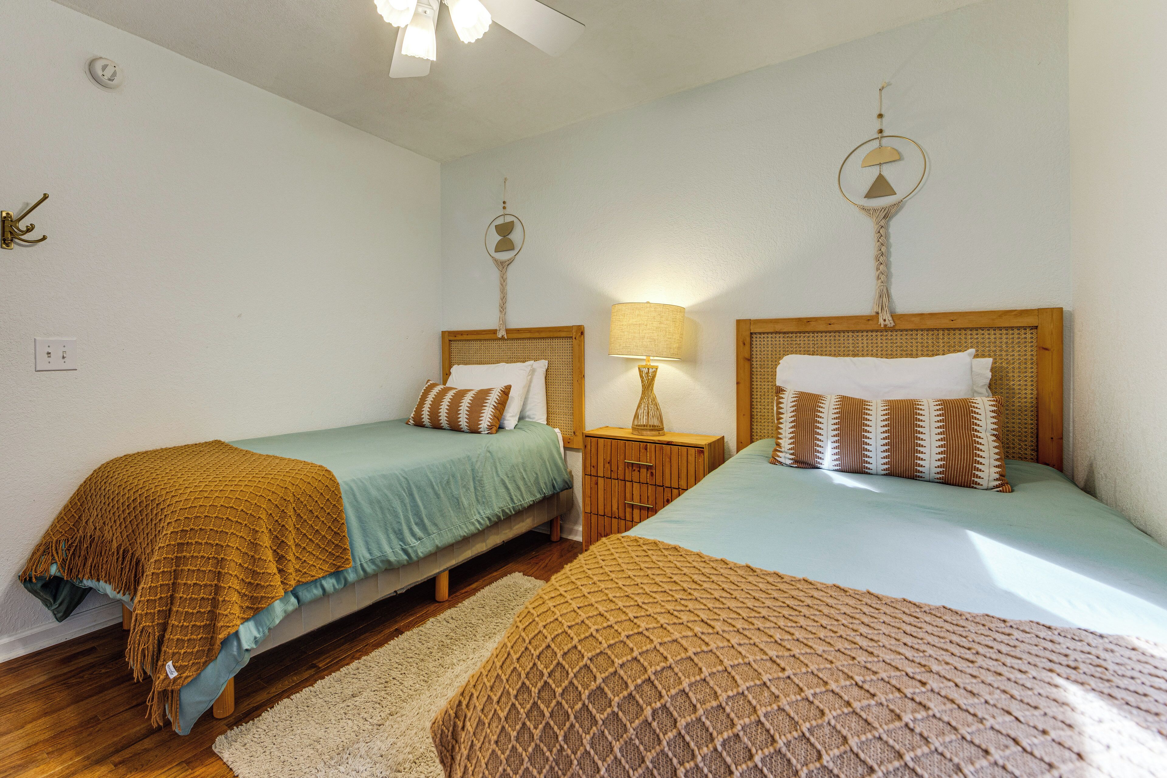 A room with two beds, a wooden nightstand, a lamp, and a wall-mounted decoration.