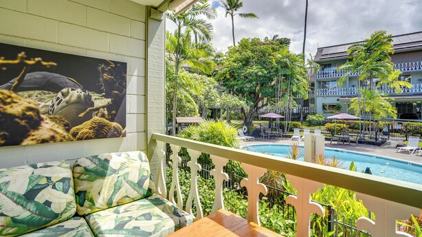 A balcony with a view of a swimming pool, lush greenery, and a building with a blue and white facade.