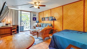 A hotel room with a bed, a sofa, a dining table, a chair, a ceiling fan, and a view of the outdoors.