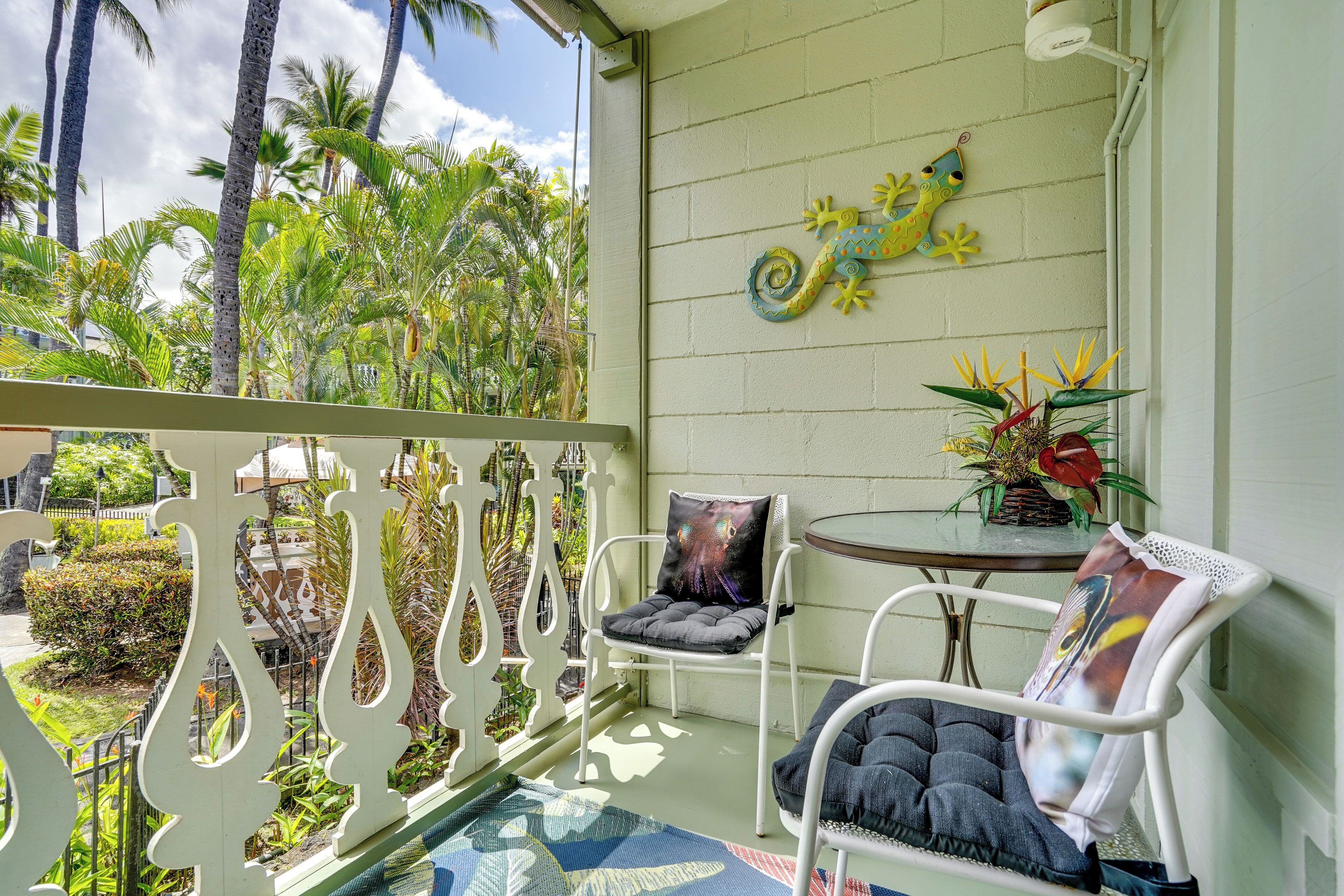 A balcony with white metal chairs, a small round table with a plant, and a decorative lizard wall art.