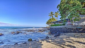 A beach with a stone wall, palm trees, and a building with a blue roof.
