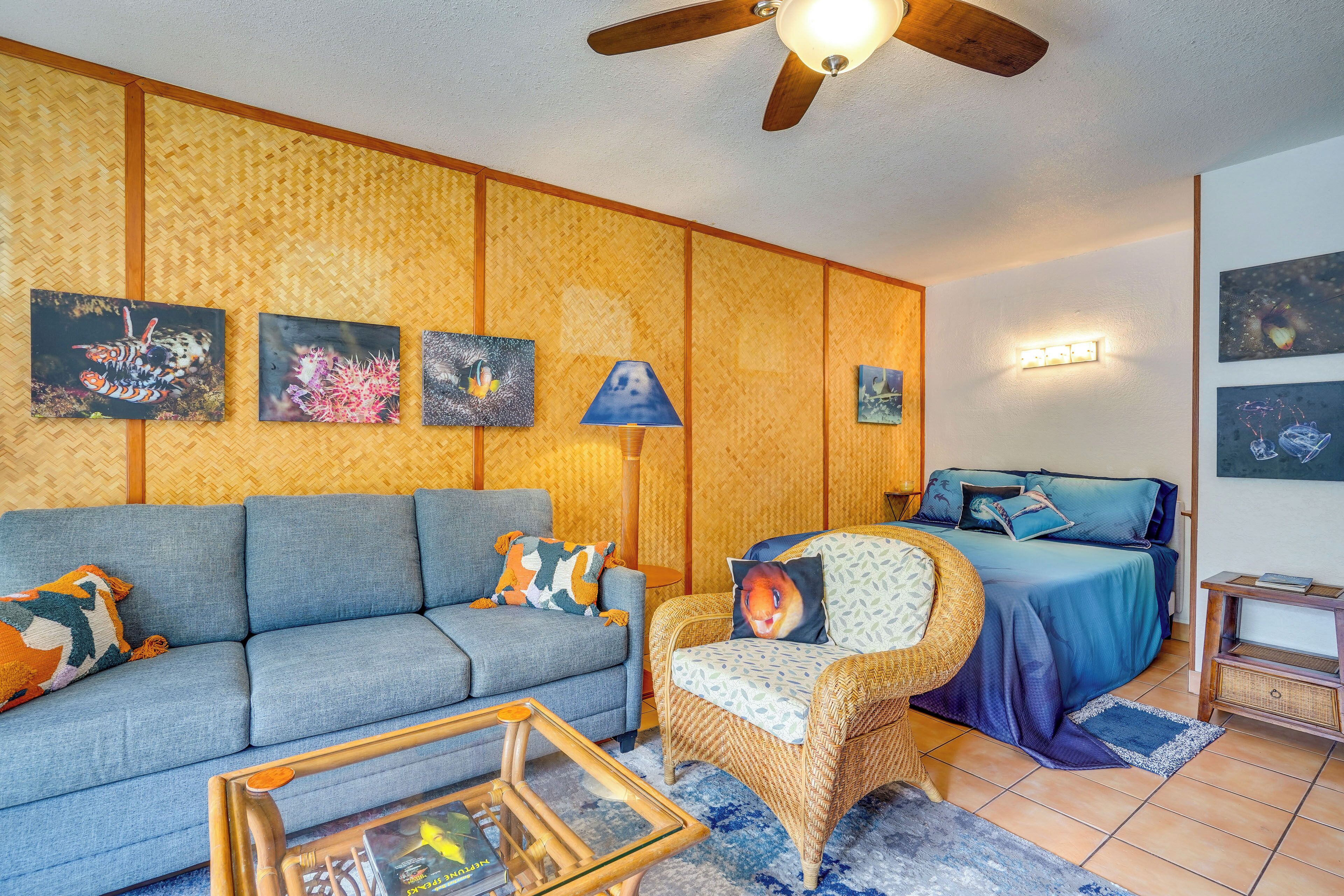 A living room with a sofa, chair, and bed, with artwork on the wall and a ceiling fan.