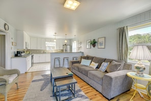 A modern living room with a grey sofa, a wooden coffee table, and a dining area with white cabinetry and a kitchen island.