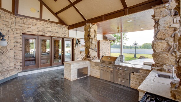 A spacious kitchen with a stone accent wall, a built-in grill, and a large window offering a view of the outdoors. - Outdoor Pool & Lake: Massive Texas Ranch Villa! (Commerce)