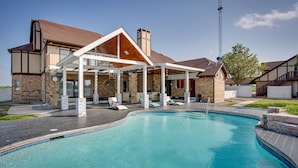 A swimming pool with a covered patio area, stone walls, and a clear blue sky. - Outdoor Pool & Lake: Massive Texas Ranch Villa! (Commerce)