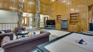 A spacious living room with a stone pillar, leather sofas, a pool table, and wooden paneling. - Outdoor Pool & Lake: Massive Texas Ranch Villa! (Commerce)