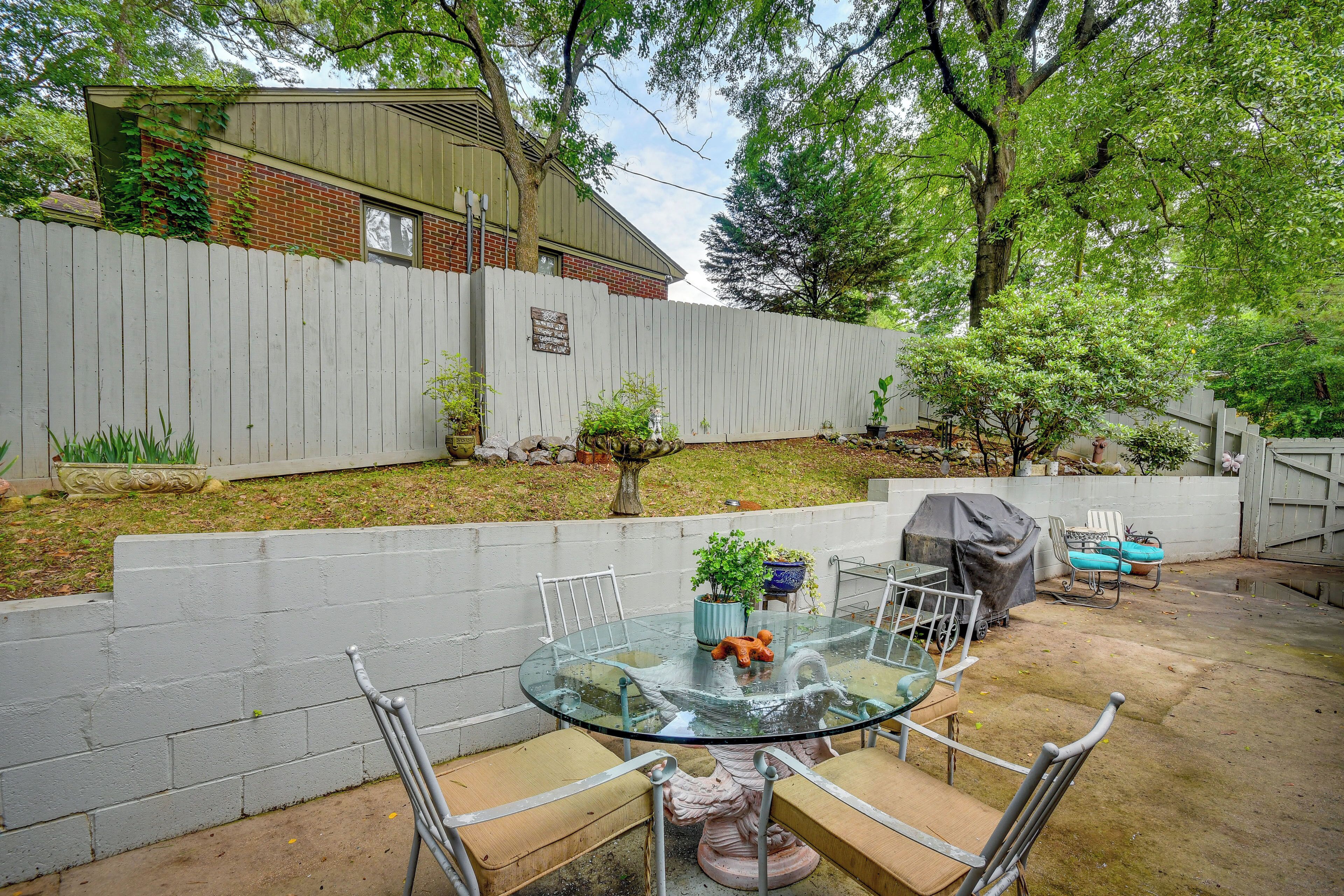 A backyard with a glass table and chairs, a barbecue grill, and a white fence.