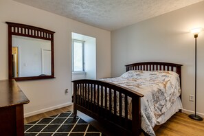 A bedroom with a wooden bed, a nightstand, a mirror, and a floor lamp. - Lawrence Vacation Rental ~ 12 Mi to Indianapolis! (Indianapolis)