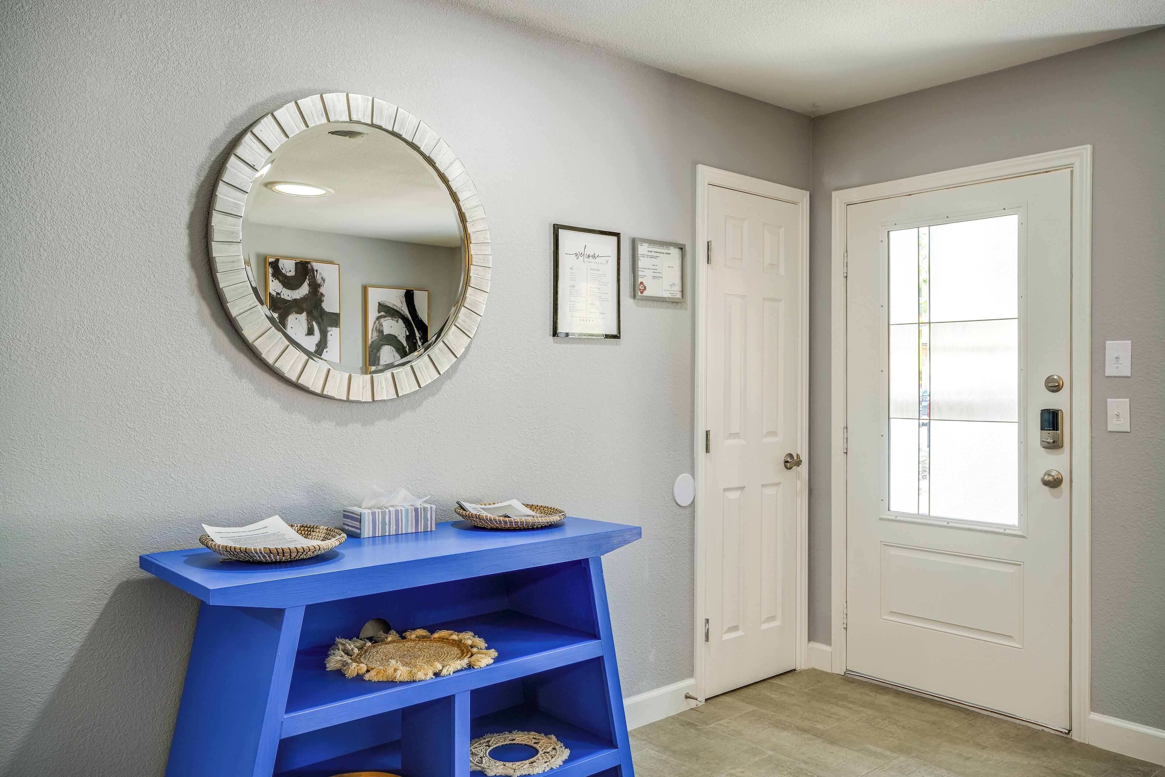 A hallway with a blue console table, a round mirror, and a white door with a window.