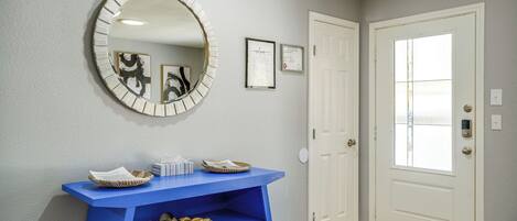 A hallway with a blue console table, a round mirror, and a white door with a window.