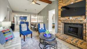 A living room with a fireplace, blue chairs, a round table, and a television mounted on the wall. - Serene San Antonio Vacation Home w/ Smart TVs (San Antonio)