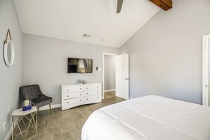 Quarto com cama, cômoda, cadeira, televisão e porta.