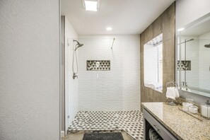 Uma casa de banho moderna com chuveiro, toucador com espelho e chão com padrão.