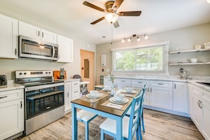A modern kitchen with white cabinets, a built-in oven, a microwave, and a dining area with blue chairs and a wooden table.