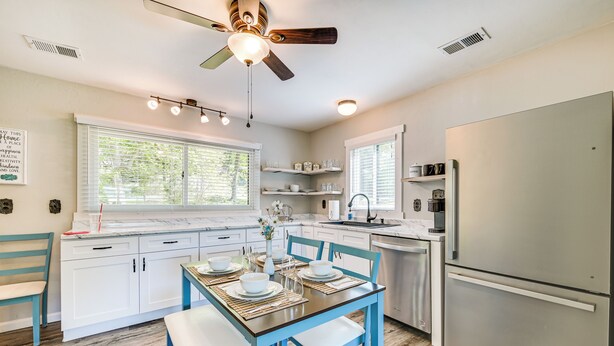 A modern kitchen with white cabinets, a stainless steel refrigerator, and a dining area with blue chairs and a wooden table. - 3 Mi to Burnside Marina: Lake Cumberland Getaway (Somerset)