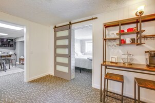 Quarto com porta deslizante que dá para um dormitório, área de cozinha com prateleiras de madeira e carpete estampado.