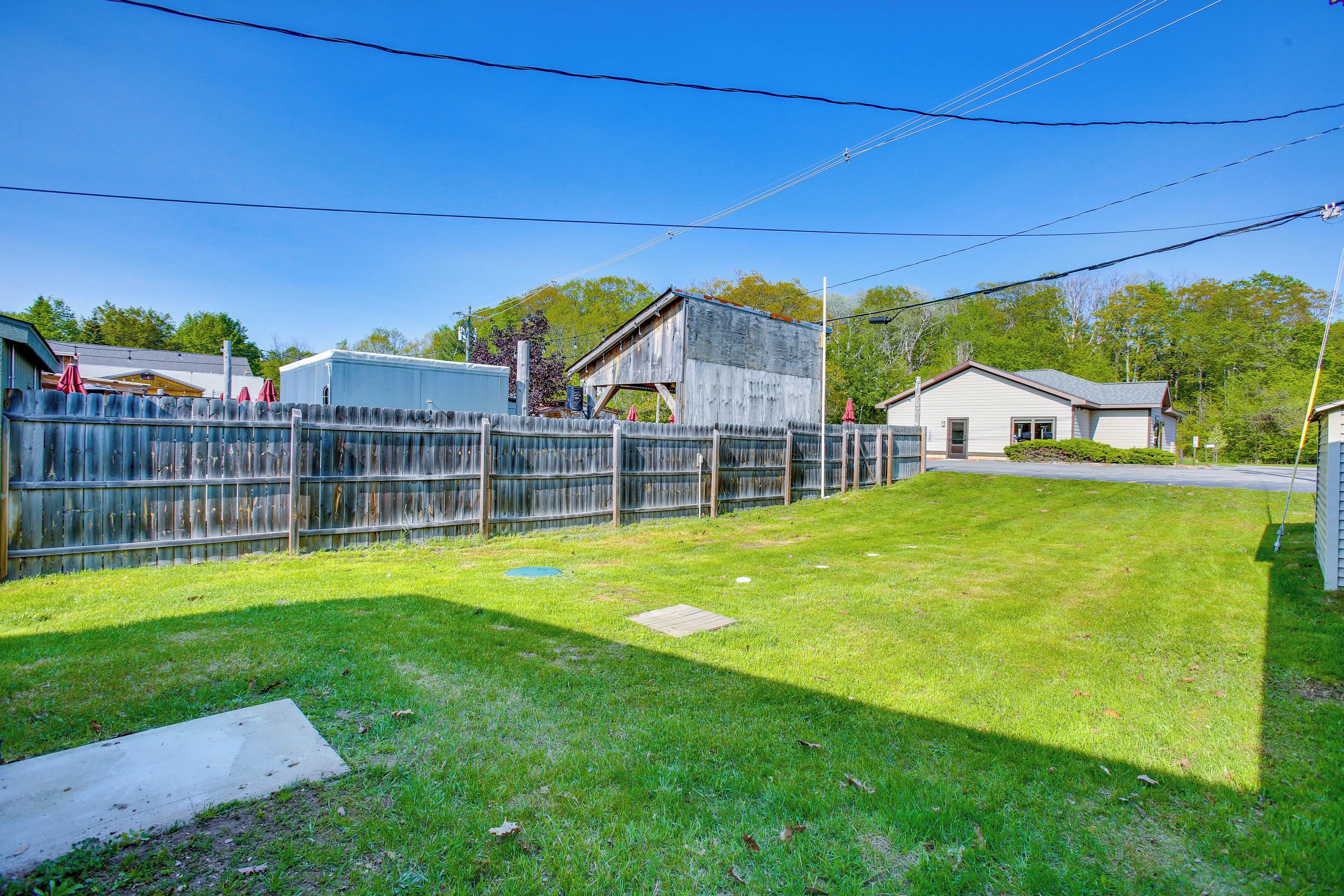 A fenced backyard with a grassy lawn, a wooden shed, and a house with a garage.