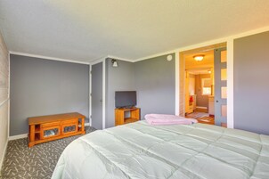 Quarto com cama, um armário de madeira, televisão e uma porta que dá para outro cômodo.