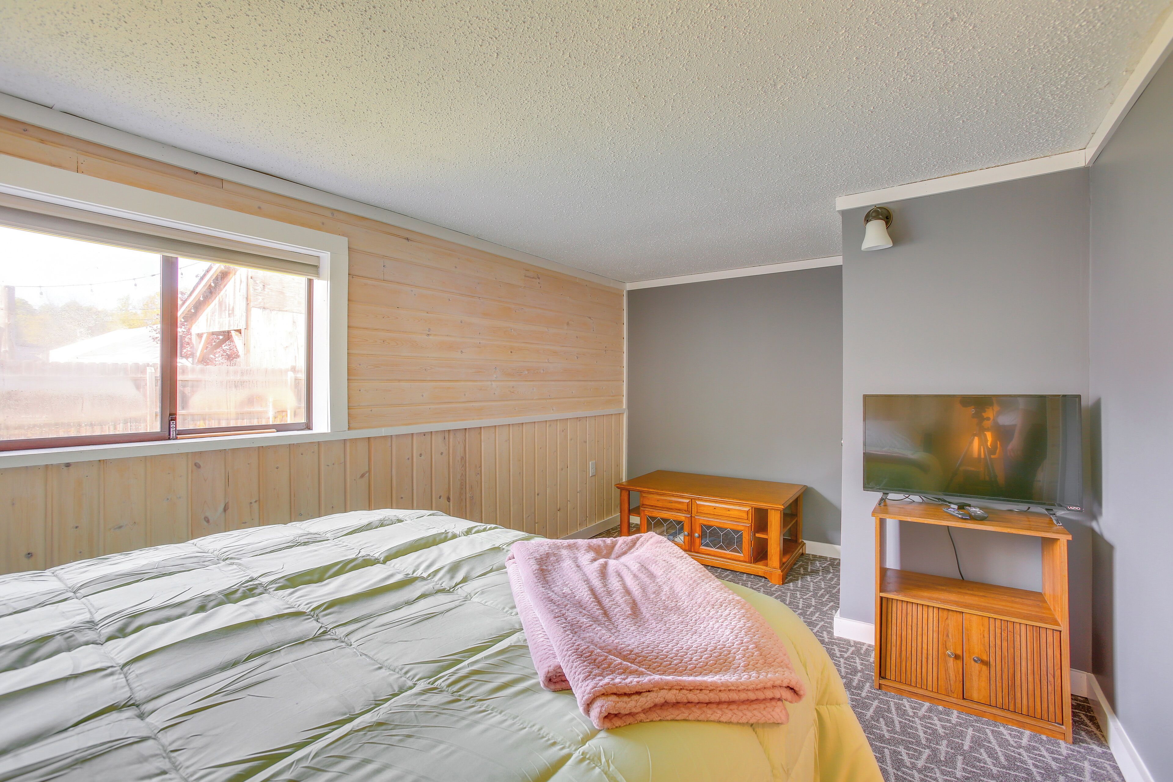 A bedroom with a bed, a wooden dresser, a television on a stand, and a window.