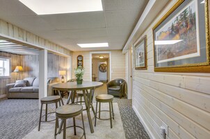 Um quarto aconchegante com piso de madeira, uma mesa redonda com banquinhos, um sofá e uma luminária.