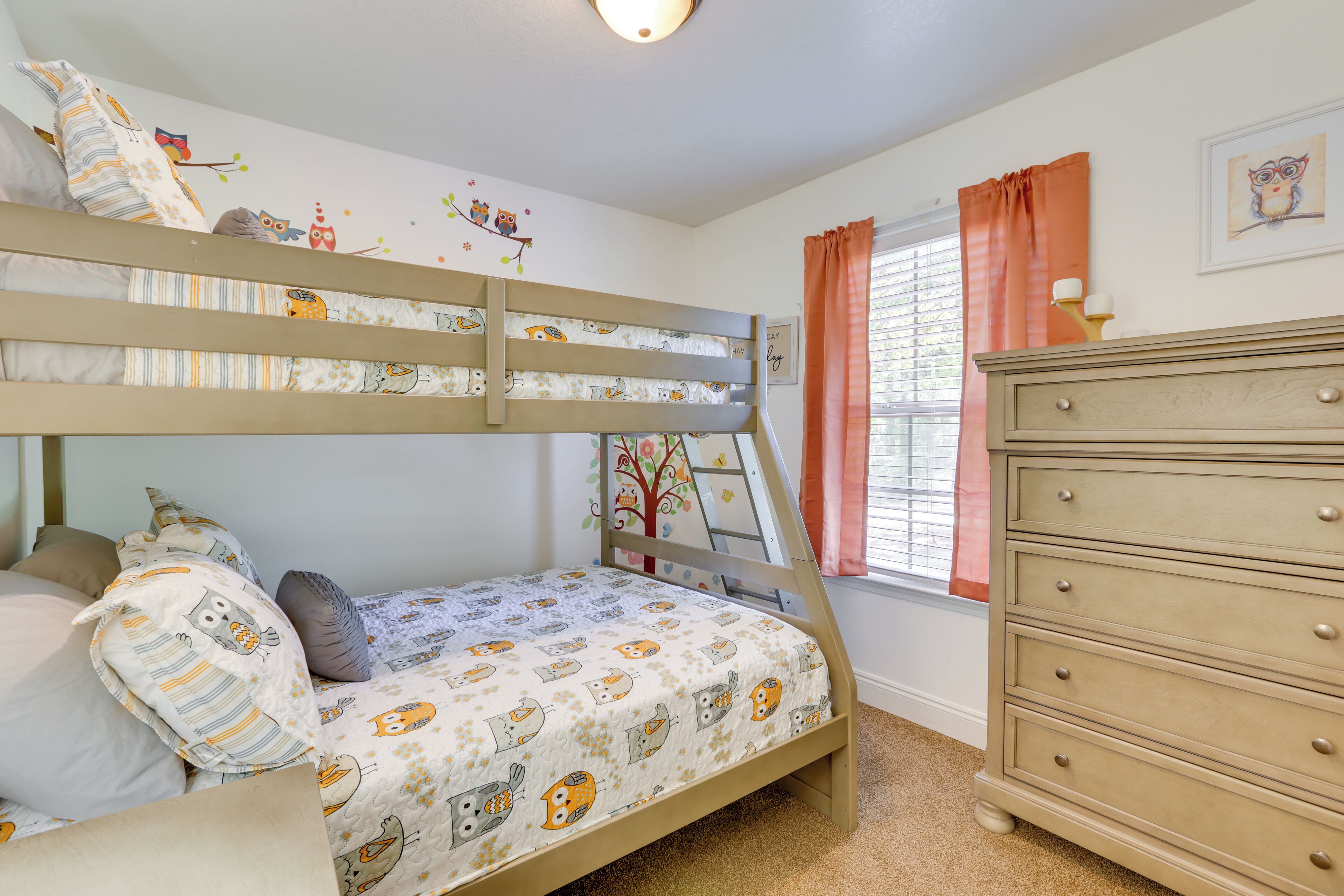 A bunk bed with a patterned bedspread, a dresser, and a window with curtains.