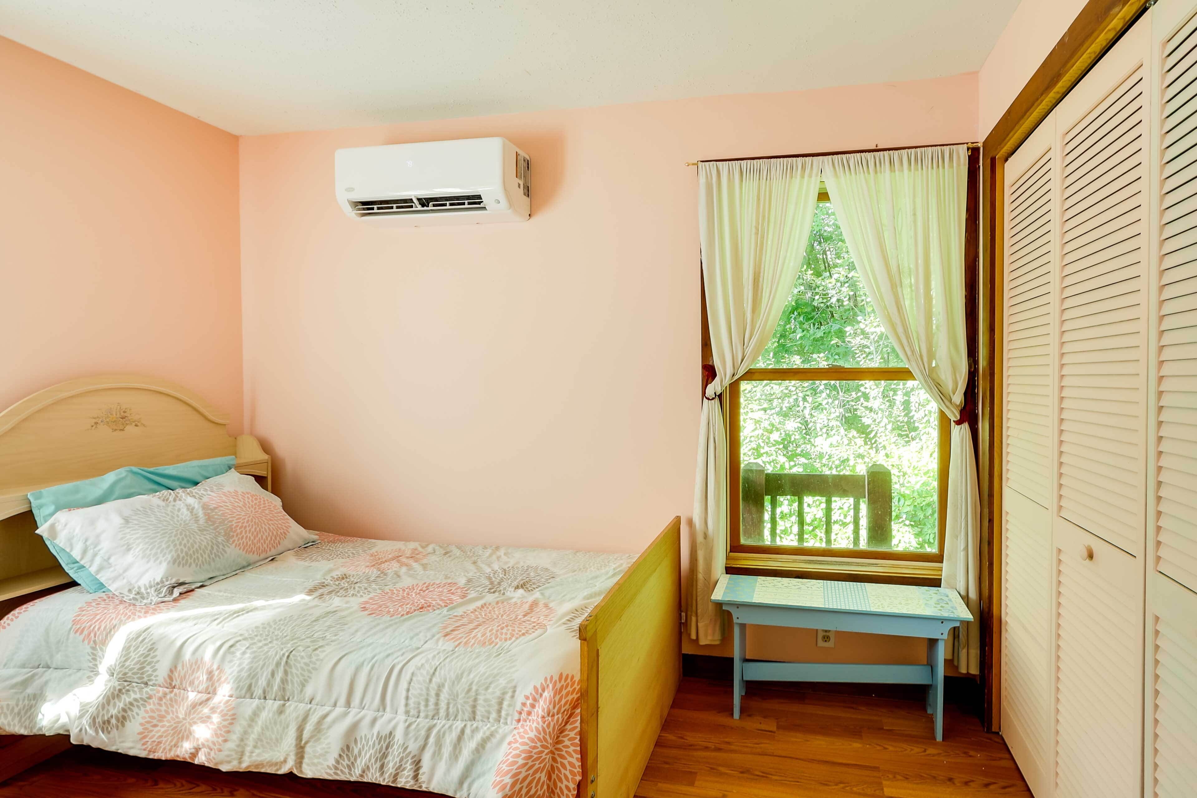 Un dormitorio con cama, ventana con cortinas, aire acondicionado y suelo de madera.