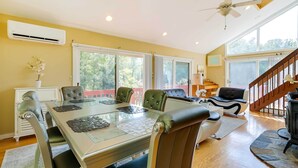 A dining area with a glass table, cushioned chairs, a ceiling fan, and a view of the outdoors through large windows.
