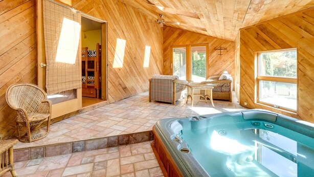 A wooden cabin interior with a hot tub, wicker furniture, and a view through a door.